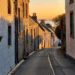 A long street of terraced Scottish houses are seen, in an eclectic mix of whitepaint and brickwork, stretching down onto a distant hillscape.