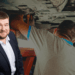 Germann Reinberg, Solicitor at Pabla & Pabla, smiles at the camera. Behind him, a car mechanic on the cusp of life-changing injuries works on the elevated underside of a vintage car.