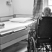 A neglected nursing home resident is seen in greyscale, looking out at their dilapidated room, wishing only that things someday might be better.