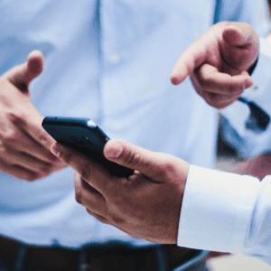 Two pairs of formally dressed hands are seen, pointing enthusiastically at a phone screen. Their owners are presumably negotiating feverishly.
