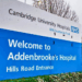 The front of Addenbrooke's Hospital is seen. Specifically, the Hills Road Entrance. The top of the central sign heralds the Cambridge University Hospitals NHS Foundation Trust. We are left to presume that Dr Kuldeep Stohr is perhaps somewhere inside.
