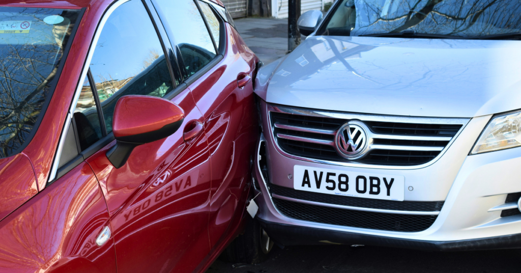 Two cars are seen, a silver Volkswagen and a mystery red car, crumpled together following a presumably nasty crash. They await the sweet embrace of the emergency services to untangle them and free them from this vehicular disaster.