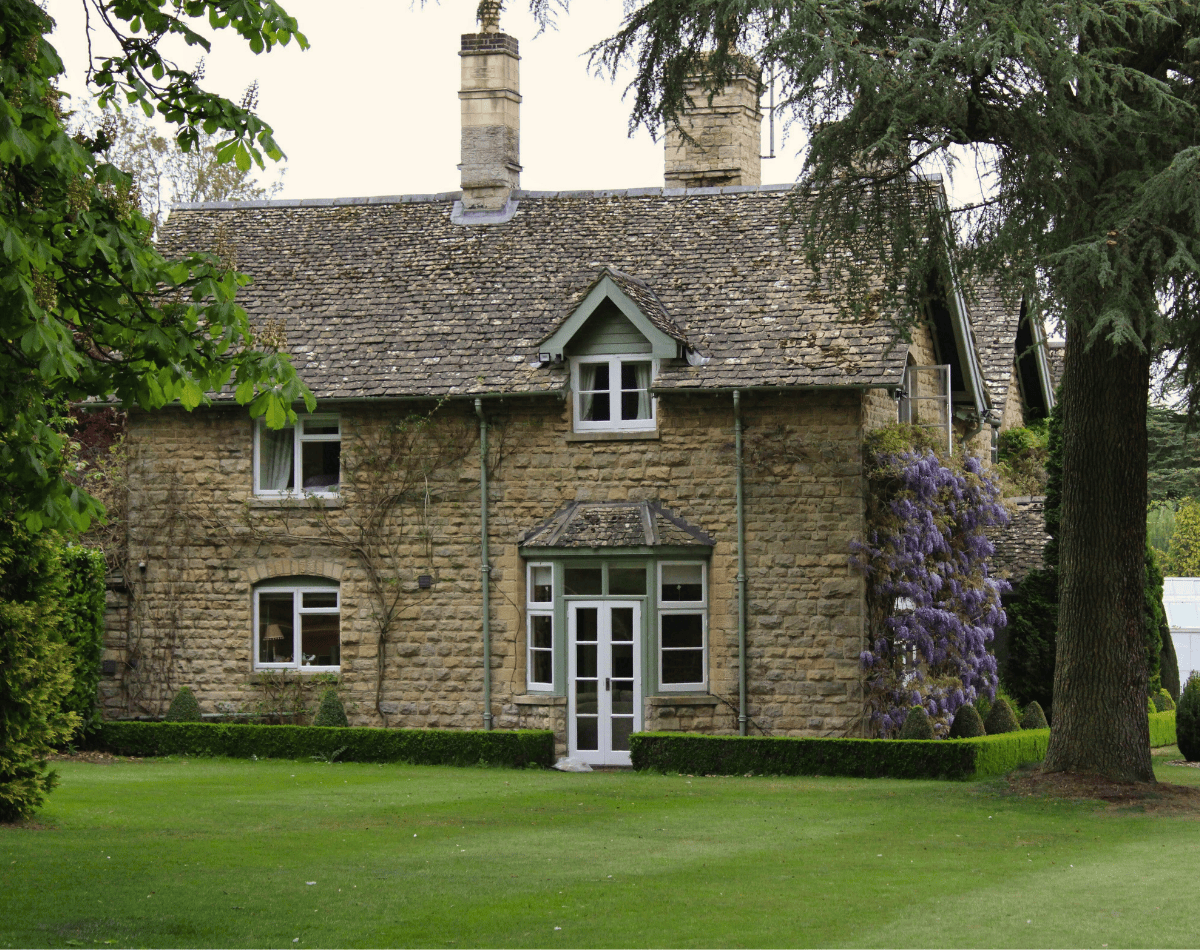 A tranquil looking sandstone cottage is seen, with an immaculately maintained lawn in stretching out before it.